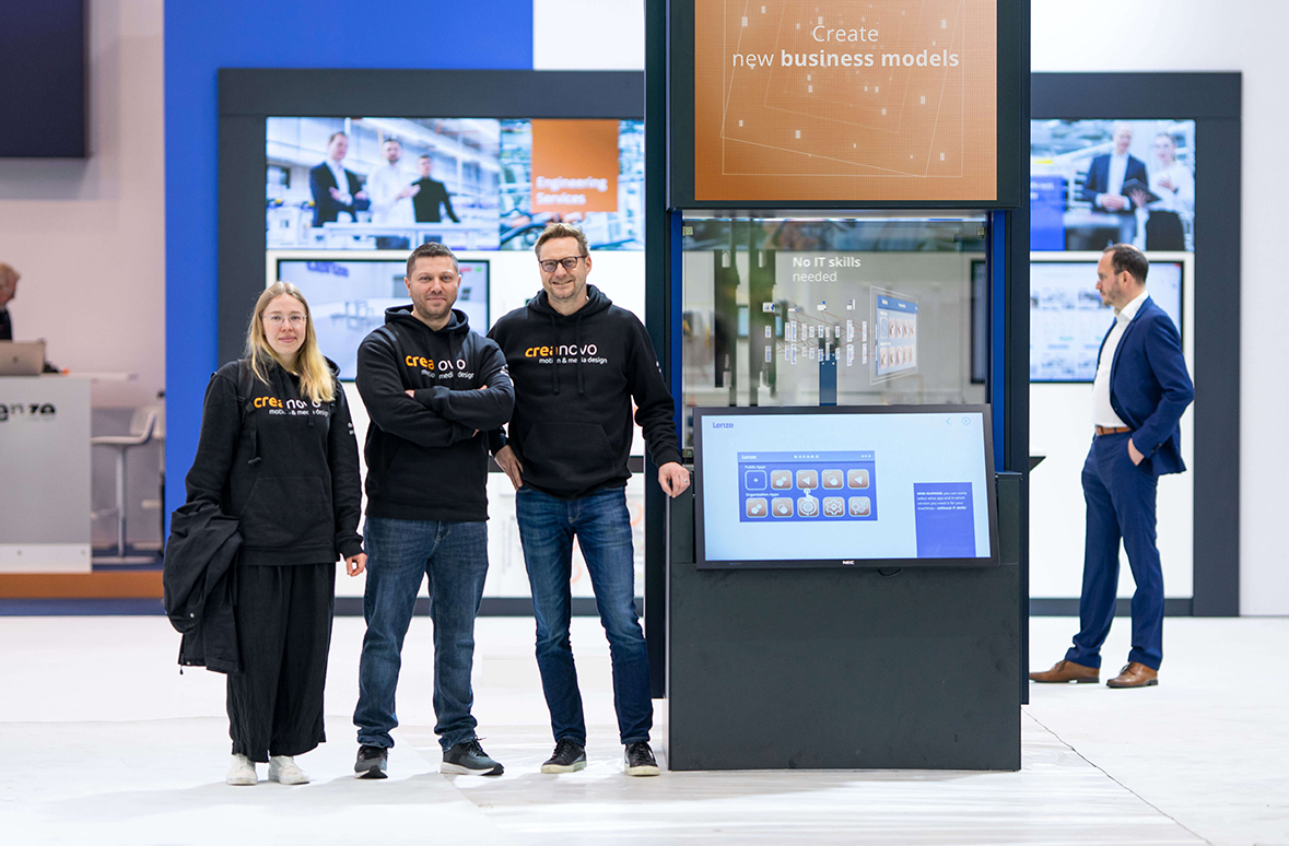 Drei Personen stehen vor einer Vitrine. Sie sind Mitglieder des creanovo Teams und befinden sich neben einem Bildschirm mit der interaktiven Anwendung, die für Lenze umgesetzt wurde.